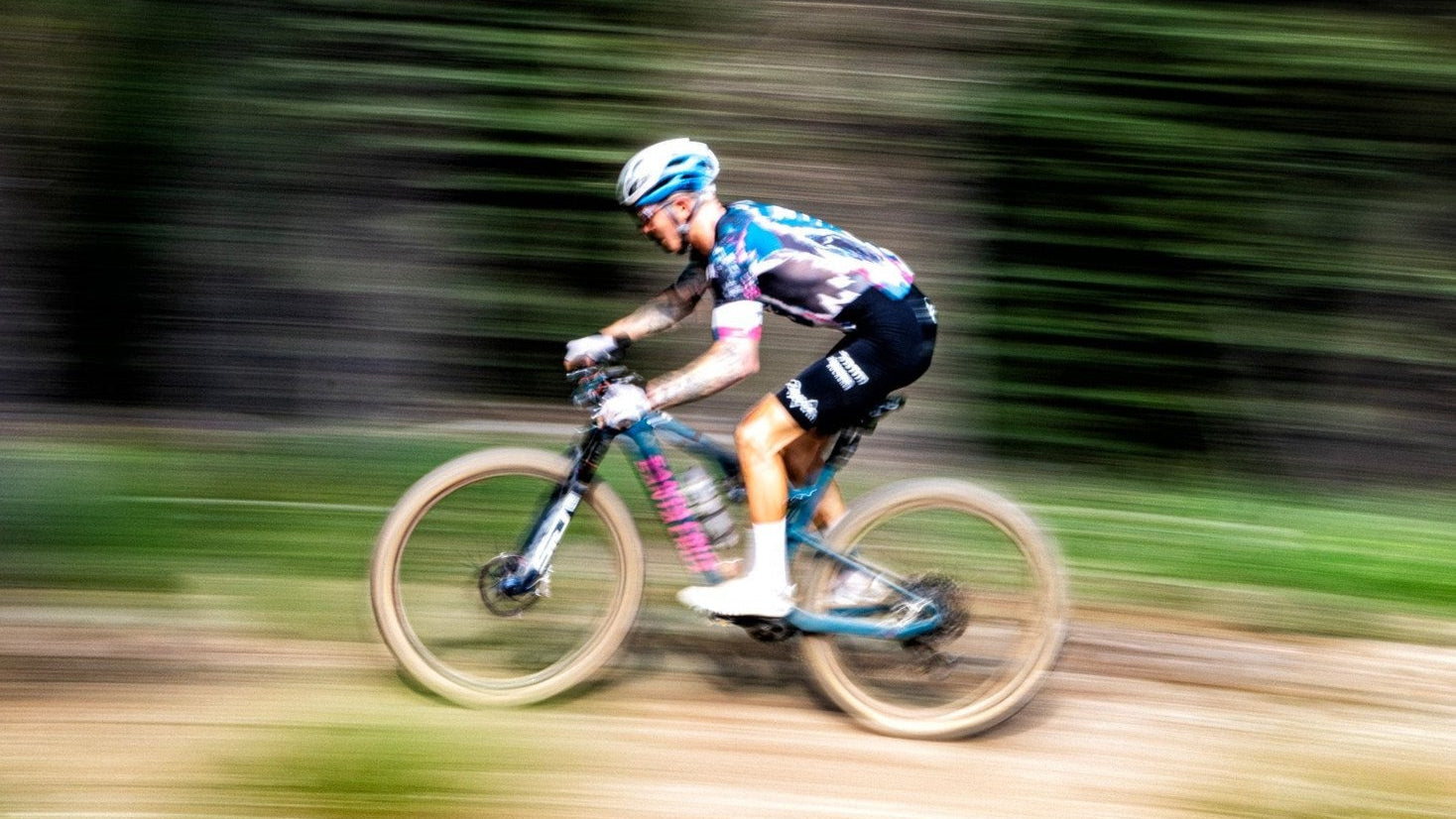 Blurred motion of a cyclist riding a mountain bike through a forest trail, capturing speed and action