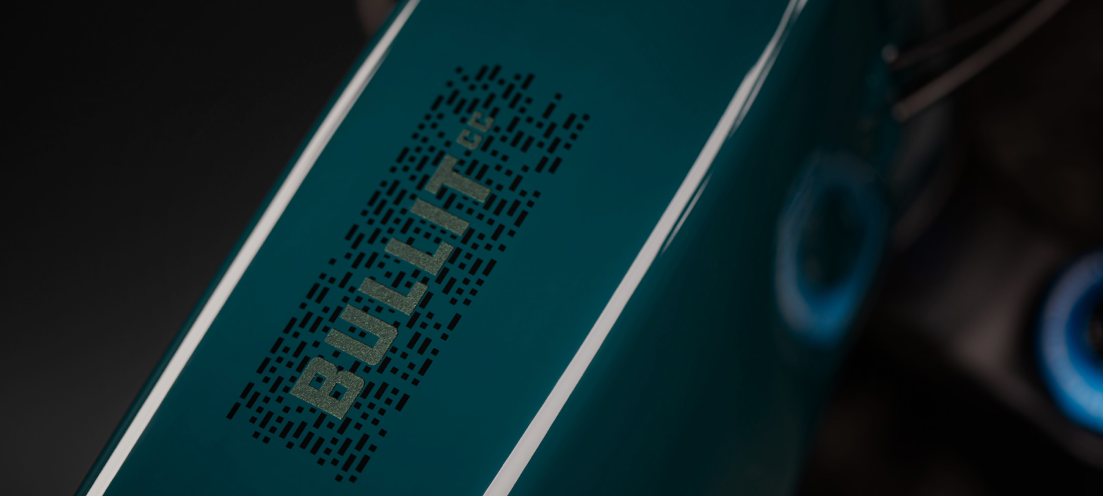 A close-up of a teal bike frame with the word "BULLIT" displayed in bold, textured lettering against a sleek finish