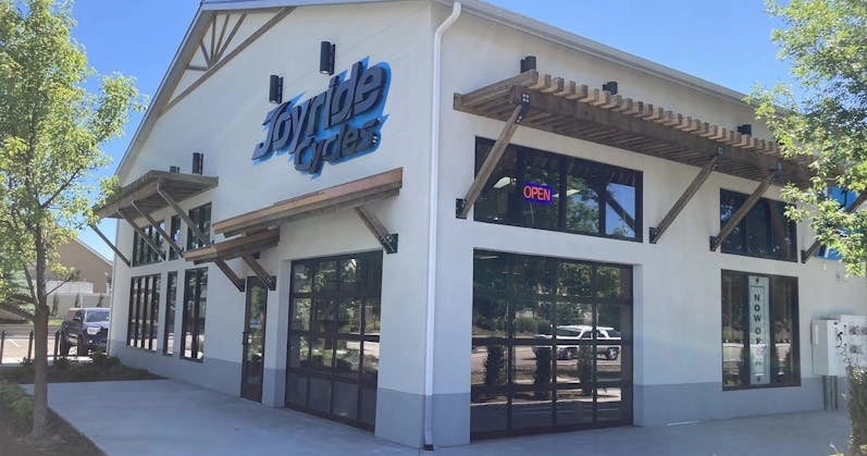 Exterior of Joyride Cycles, a modern bike shop with large windows, wooden accents, and an open sign visible