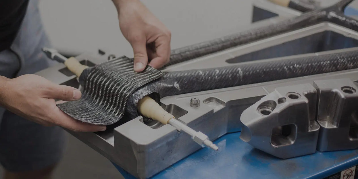 Hands meticulously position carbon fiber material on a bike frame mold, showcasing precision in the manufacturing process