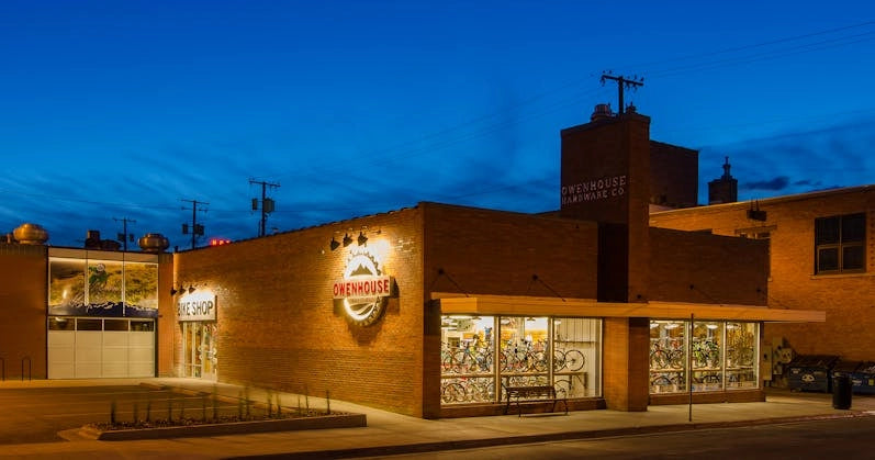 Exterior of Owenhouse Cycling at dusk, showcasing a brick building with large glass windows displaying bicycles.