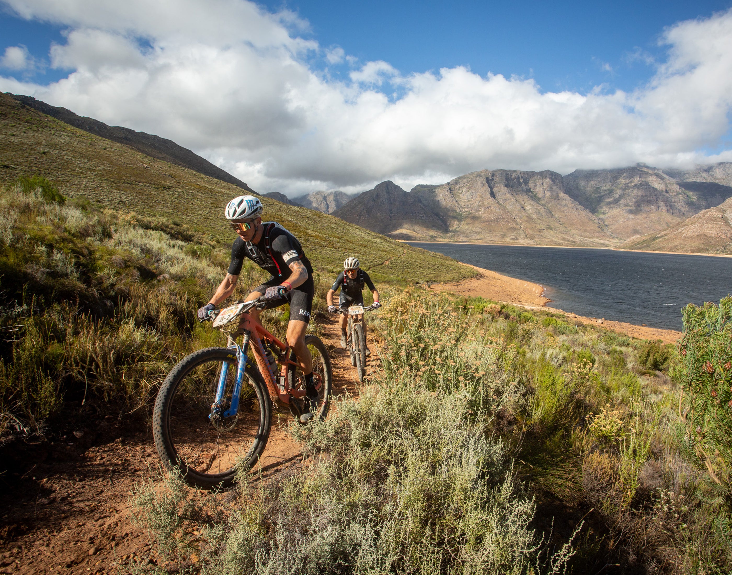 Riders pedaling up a trail near a lake