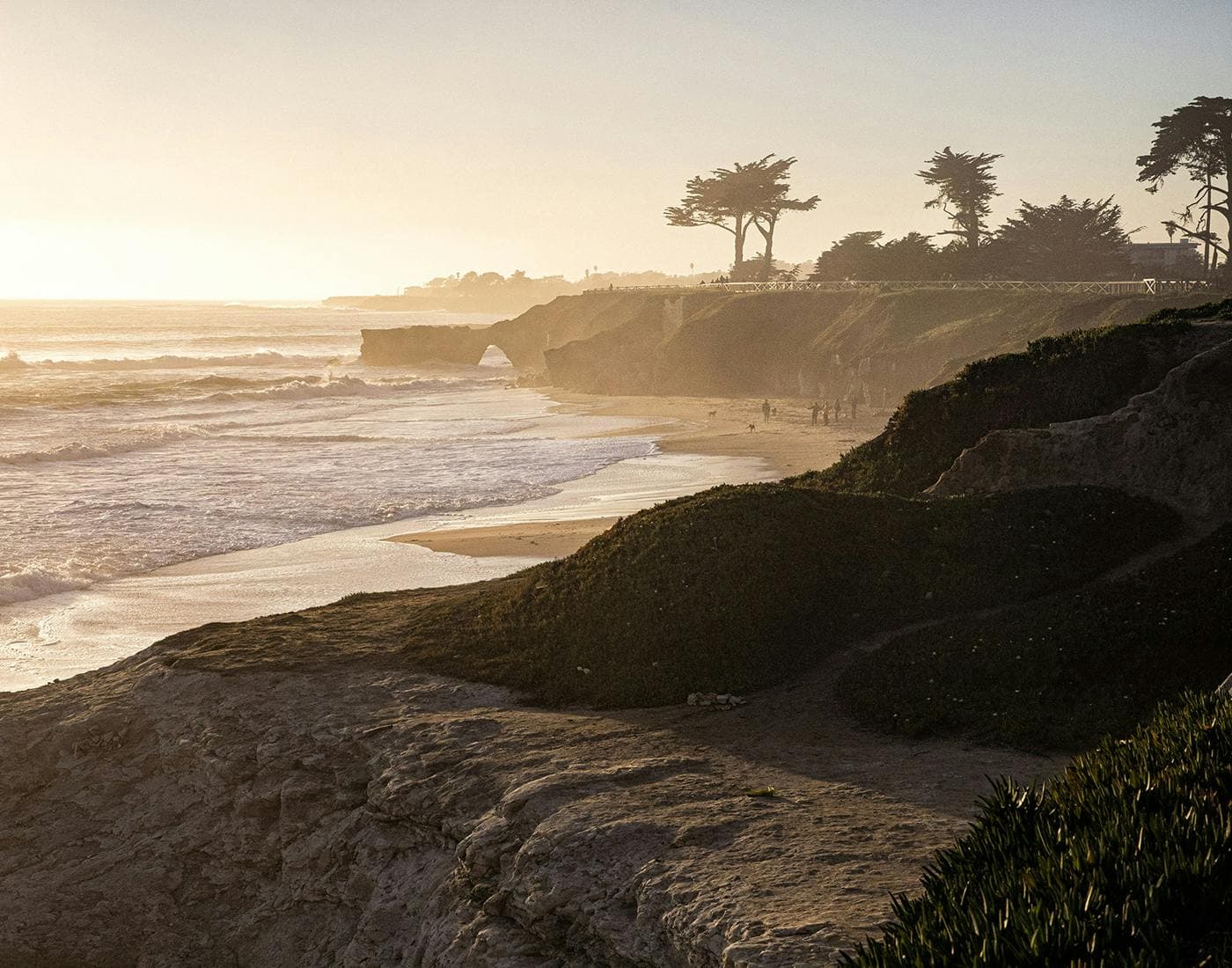 A serene coastal landscape at sunset, featuring cliffs, a sandy beach, and gentle waves under a golden sky