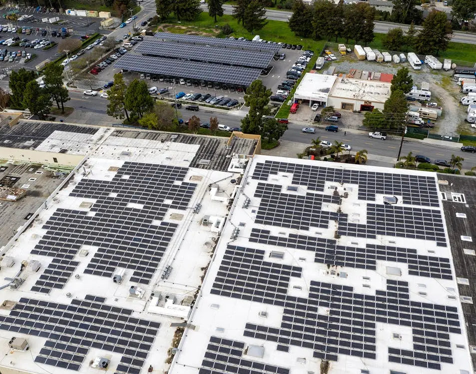 Overhead view of a large industrial building with solar panels installed on the roof and a solar parking area