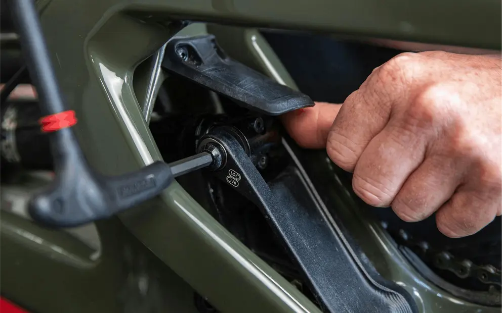 Close-up of a Santa Cruz bike frame in olive green with a hand adjusting the suspension linkage using a hex key