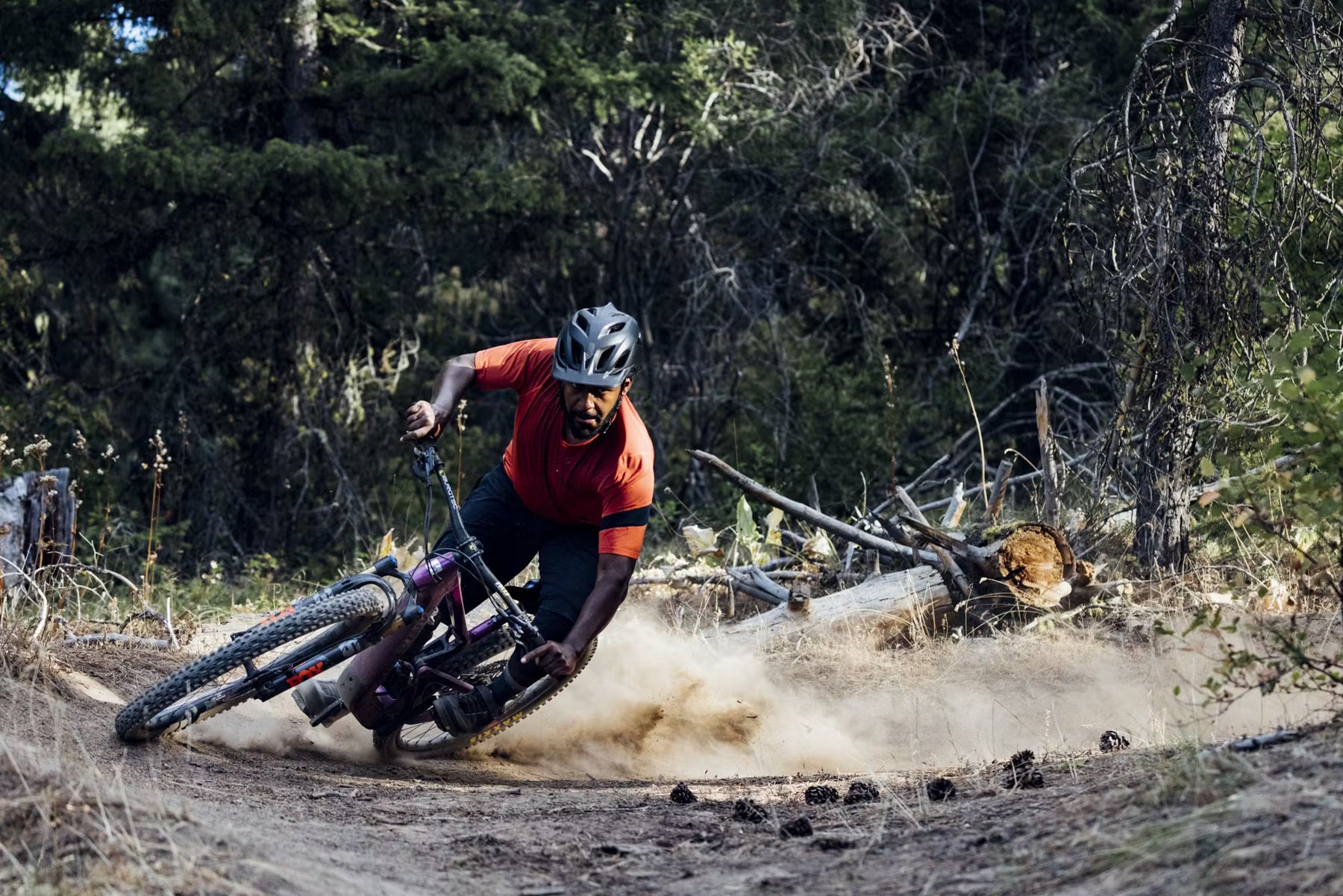 A rider carves through a dusty trail corner, demonstrating skillful control and focus amidst a forest backdrop