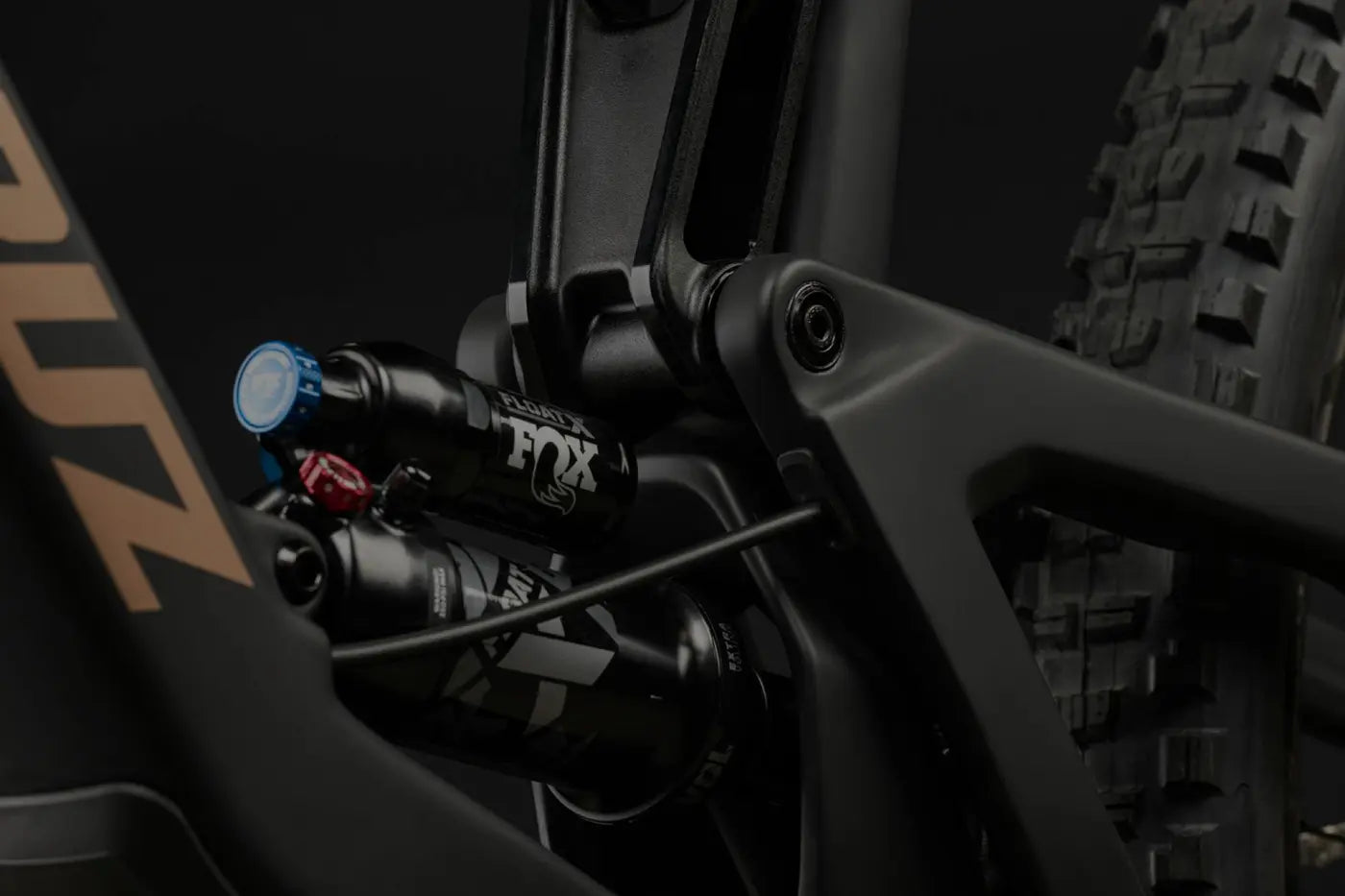 A close-up of a mountain bike's rear suspension system, highlighting the FOX Float shock absorber and linkage components against a black backdrop