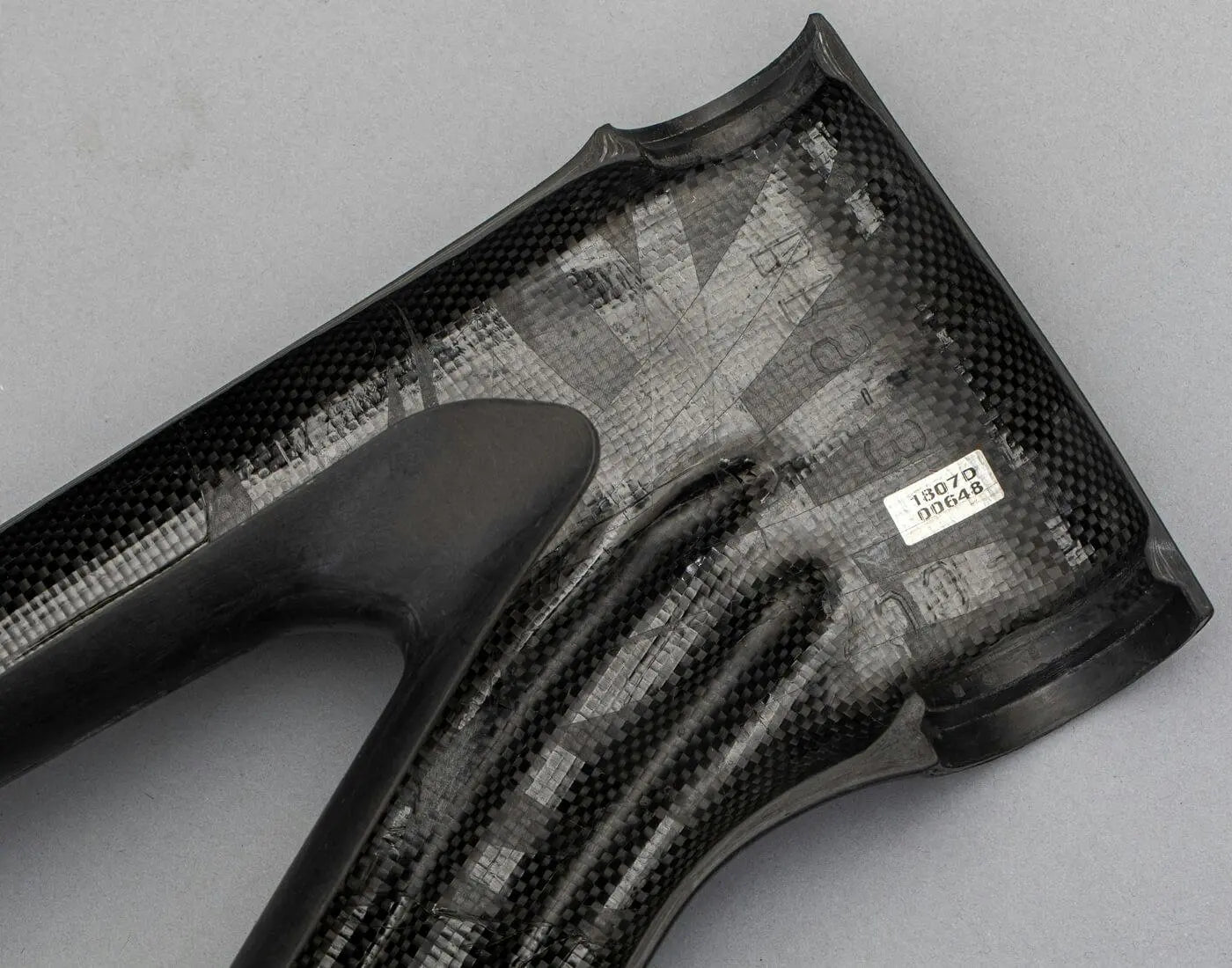 A close-up of a carbon fiber bike frame section, highlighting the intricate weave and structural integrity, with a visible identification label