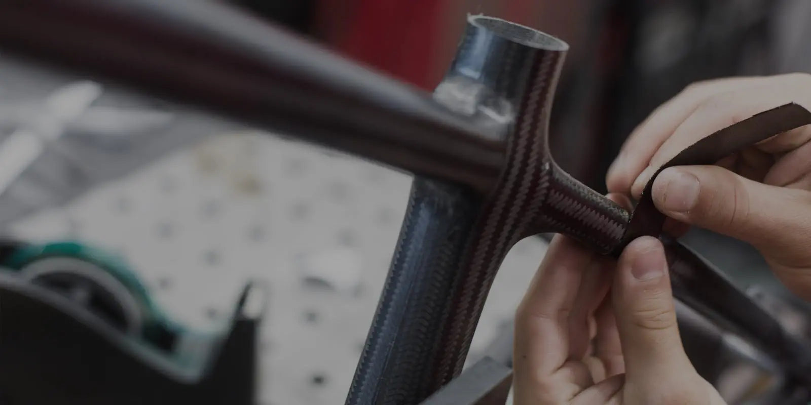 Hands carefully apply finishing touches to a carbon bike frame, showcasing craftsmanship in a workshop