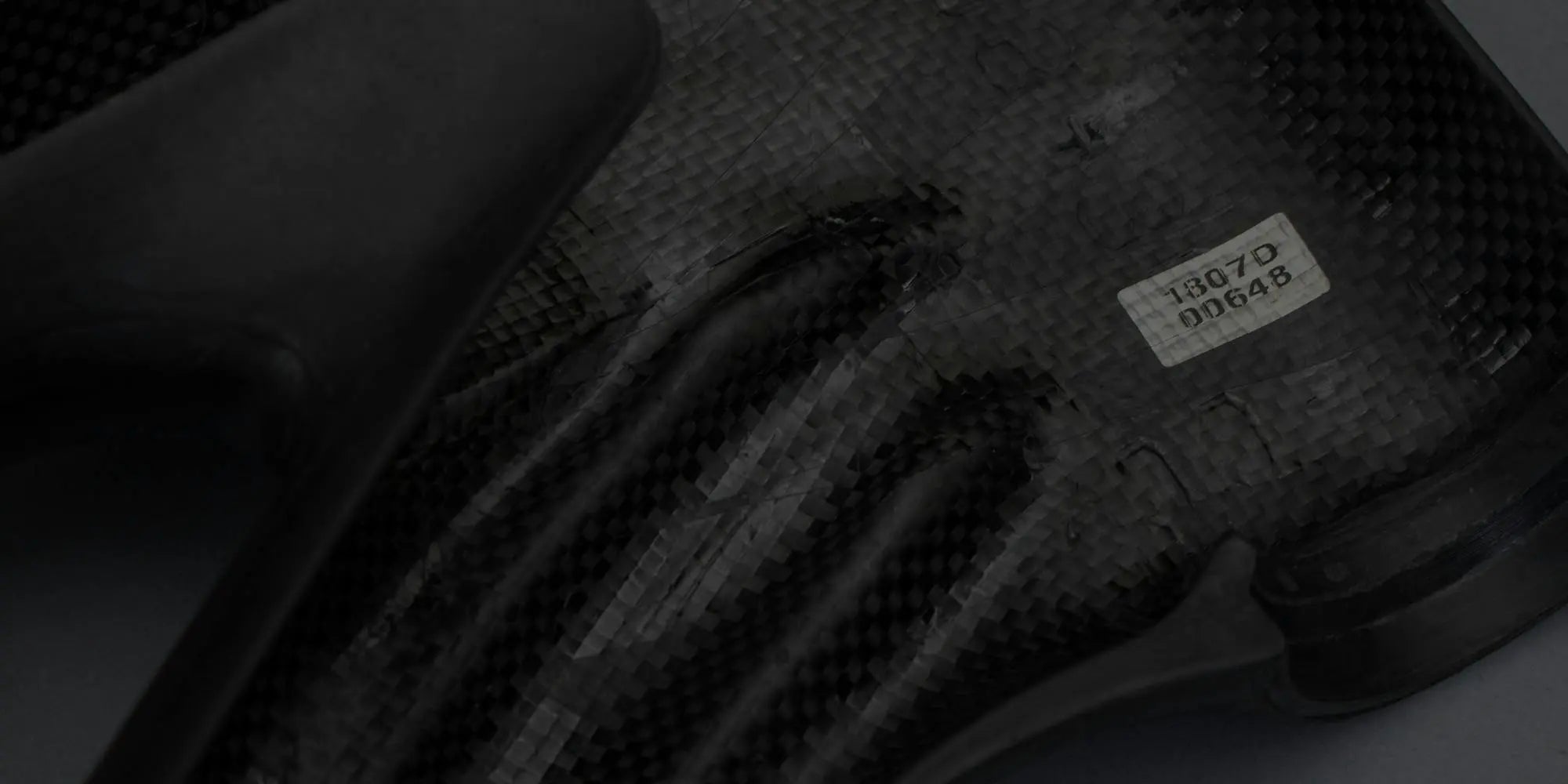 A detailed close-up of a carbon fiber bike component, showing its weave texture and a small identification label