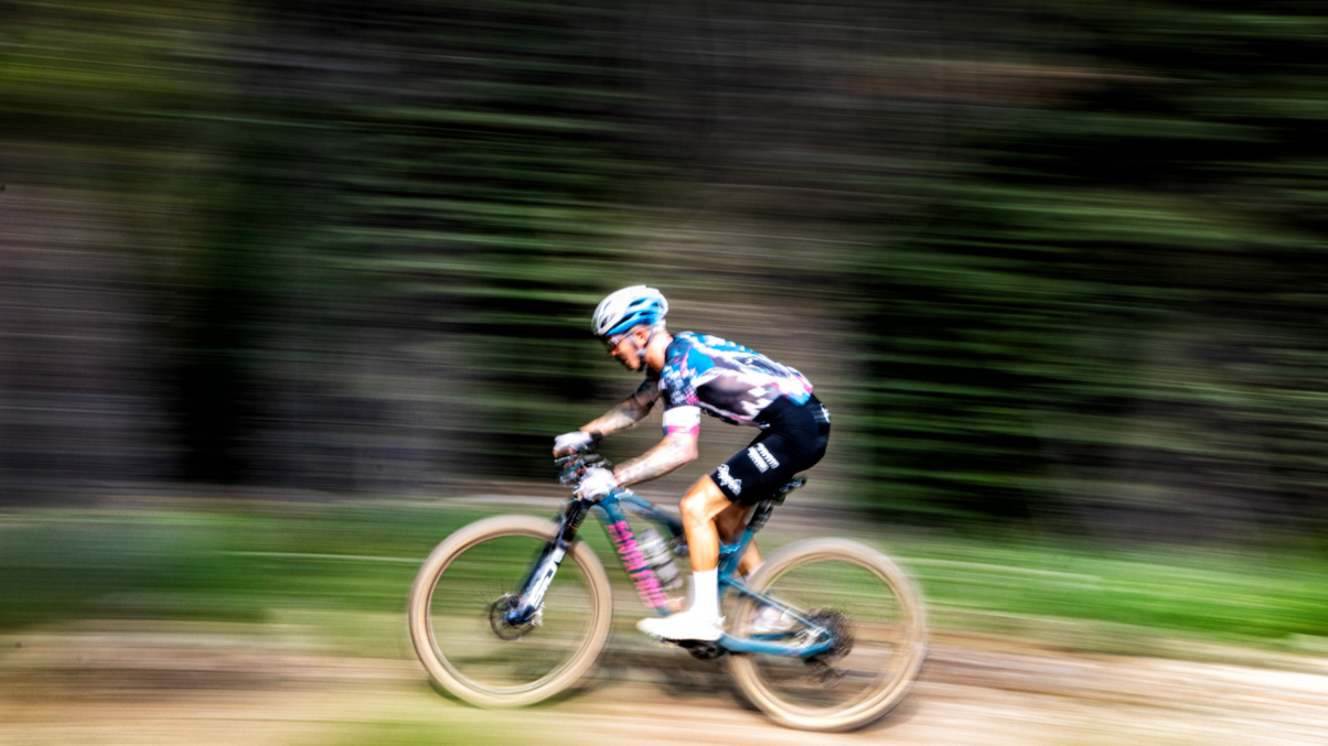 Blurred motion of a cyclist riding a mountain bike through a forest trail, capturing speed and action