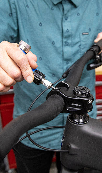 A person adjusts the stem bolts of a bike handlebar using a torque wrench in a workshop setting