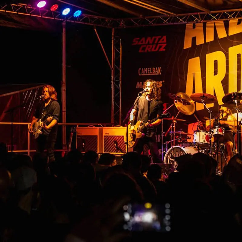 Live band performing at Aard Rock, with Santa Cruz branding and vibrant stage lights illuminating the scene